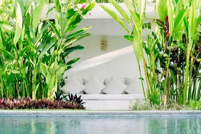 a white couch in between plants near a swimming pool at Yahira Stunning Garden 5 BR Private Pool Villa in Canggu
