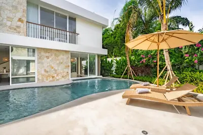a pool with two chairs and an umbrella next to a house at Villa Twin 2 by BaliSuperHost in Canggu