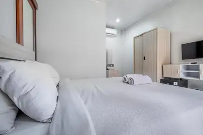 a white bedroom with a large bed and a television at Collection O Dukuh Segara Guest House in Balian