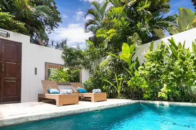 a villa with a swimming pool and two chairs next to a house at Villa Atma 2BR Fully Equipped Kitchen in Seminyak