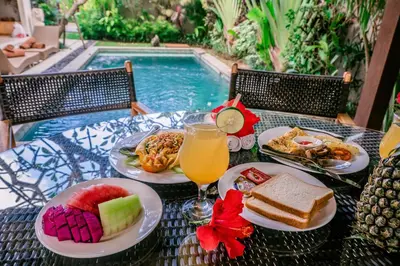 a table with plates of food next to a swimming pool at Desa Di Bali Villas in Kerobokan