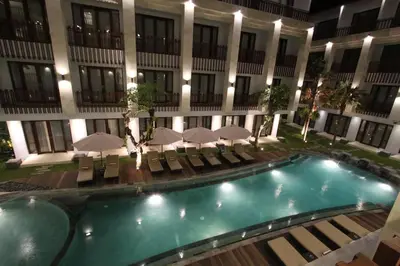 a pool in front of a building with chairs and umbrellas at Grand La Walon Hotel in Legian