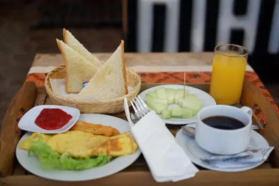 a tray with a plate of breakfast food and a cup of orange juice at Akatara Stay in Jimbaran