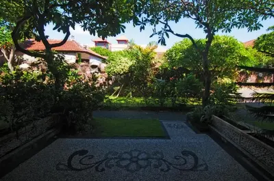 a garden in front of a building with trees at Pesona Beach Inn in Kuta