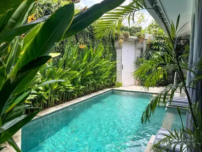 a swimming pool in a garden with green plants at Villa Ozamiz Seminyak in Seminyak