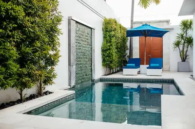 a swimming pool with two blue chairs and an umbrella at Kamil Villas in Seminyak
