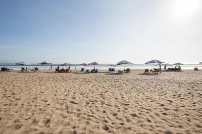 a beach with umbrellas and people sitting on the sand at Away Bali Legian Camakila in Legian