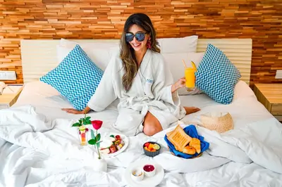 a woman sitting on a bed with food and a drink at Away Bali Legian Camakila in Legian