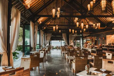 a restaurant with tables and chairs and windows at Jimbaran Puri, A Belmond Hotel, Bali in Jimbaran