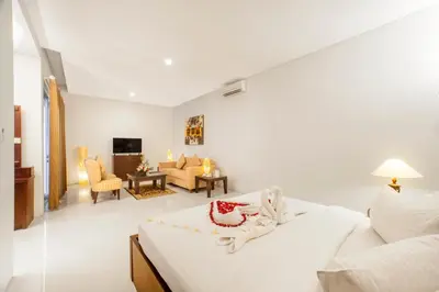 a white bedroom with a bed and a living room at The Radiant Hotel in Kuta