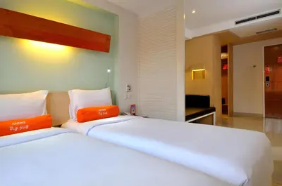 a bedroom with two white beds with orange pillows at HARRIS Hotel & Residences Riverview Kuta, Bali in Kuta