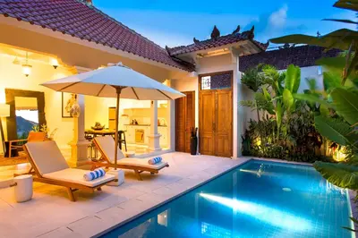 a pool with chairs and an umbrella next to a house at Villa Soleh in Seminyak