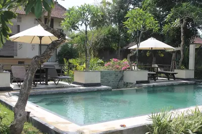 a swimming pool with tables and umbrellas in a yard at Puri Kutat Lestari in Sanur