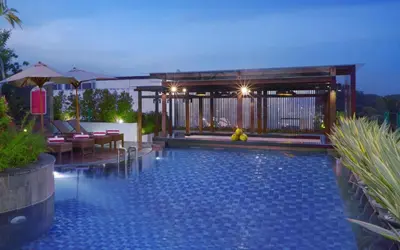 a swimming pool with chairs and umbrellas at night at favehotel Kuta Kartika Plaza in Kuta