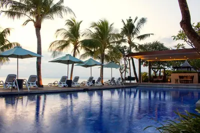 a swimming pool with chairs and umbrellas and palm trees at The Anvaya Beach Resort Bali in Kuta