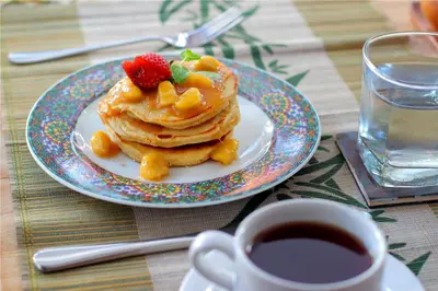 a plate of pancakes with a strawberry on top and a cup of coffee at Sleepwell Seminyak in Seminyak