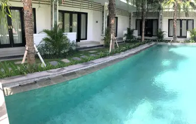 a swimming pool in front of a house with blue water at Indah Homestay in Seminyak