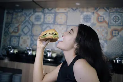 a woman eating a sandwich in a kitchen at Fame Hotel Sunset Road in Kuta