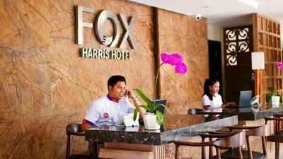 a man sitting at a table talking on a cell phone at FOX Hotel Jimbaran Beach Bali in Jimbaran