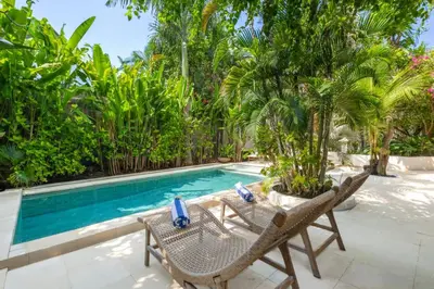 a resort pool with two chairs and palm trees at Ocean Star 5 in Seminyak