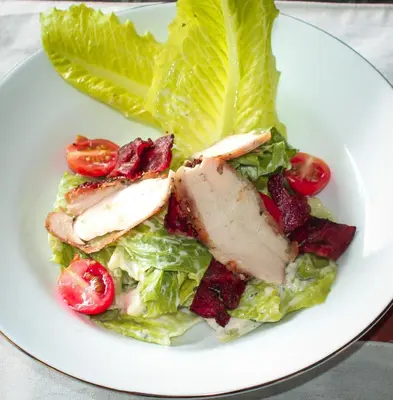 a white plate with a salad with chicken lettuce and tomatoes at The Diana Suite in Kuta