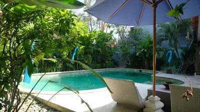 an umbrella and chairs next to a swimming pool at Villa Alam Biru Gardenia in Seminyak