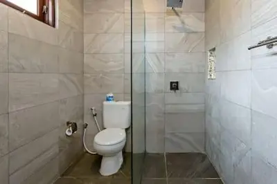 a bathroom with a toilet and a glass shower at Villa Tiah in Kuta