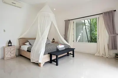 a bedroom with a canopy bed with a table and a window at Villa Niluh in Canggu
