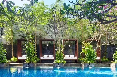 a pool at a resort with white chairs and trees at Jambuluwuk Oceano Seminyak Hotel in Seminyak