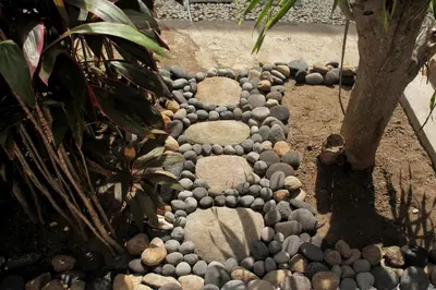 a walkway made out of rocks next to a tree at Nuka Beach Inn in Kuta