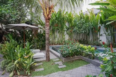 a garden with a palm tree and a swimming pool at Dee Mansion Bali in Denpasar