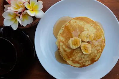 a white plate with pancakes with bananas on top at D'Pande Kuta in Kuta