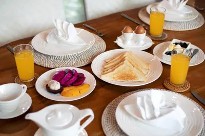 a wooden table with plates of breakfast foods and orange juice at Villa Du Ho by Villa Finder in Kerobokan