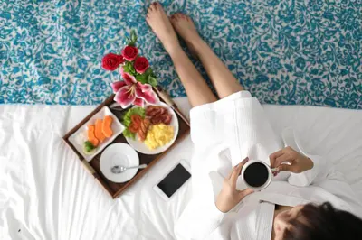 a woman laying in bed with a tray of food and a breakfast at Mahana Living in Denpasar
