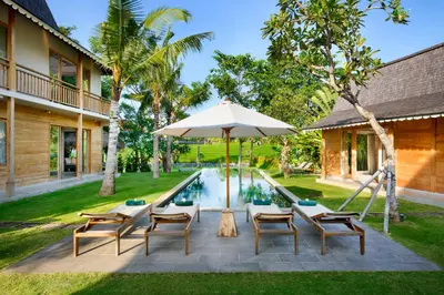 a pool with chairs and an umbrella next to a house at Alea Estate in Kerobokan