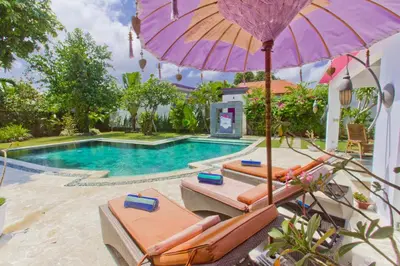 a pool with chairs and an umbrella and a swimming pool at Villa Purple in Legian