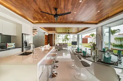 a kitchen with a long bar with chairs and a ceiling at Villa Kamag Seminyak in Seminyak
