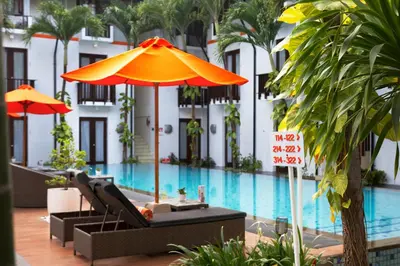 a hotel with a pool and an orange umbrella and chairs at HARRIS Hotel Kuta Tuban Bali in Kuta