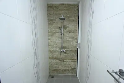 a shower in a bathroom with a brick wall at Tom Guest House in Legian