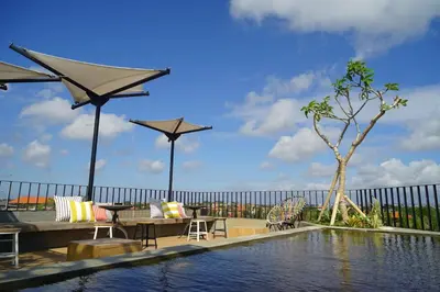 a swimming pool with tables and chairs and umbrellas at Borough Capsule Hostel Bali in Legian