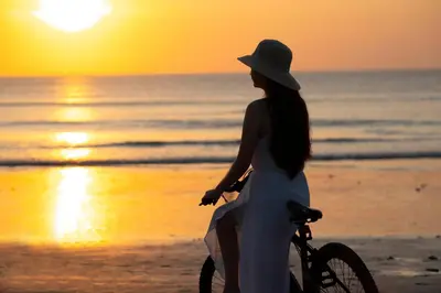 a woman riding a bike on the beach at sunset at Kayumanis Jimbaran Private Villas & Spa in Jimbaran
