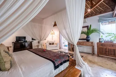 a bedroom with a large bed with white curtains at Baby Melon Villas in Seminyak