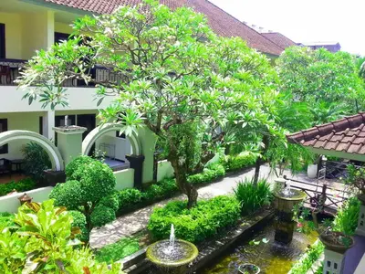 a garden with a tree and a pond in front of a building at Legian Paradiso Hotel in Legian