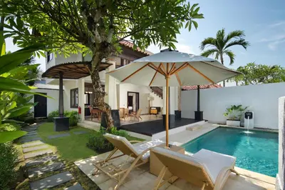 a pool with chairs and an umbrella next to a house at The Club Villas Seminyak in Seminyak