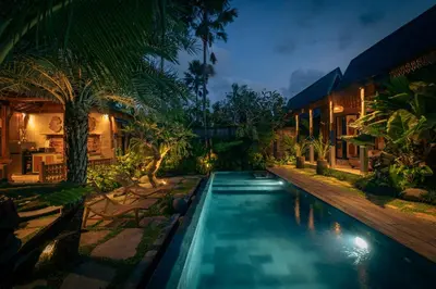 a swimming pool in front of a house at night at Kubu Kayu Villas in Seminyak