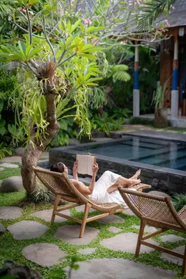 a person laying in a chair reading a book at Kubu Kayu Villas in Seminyak
