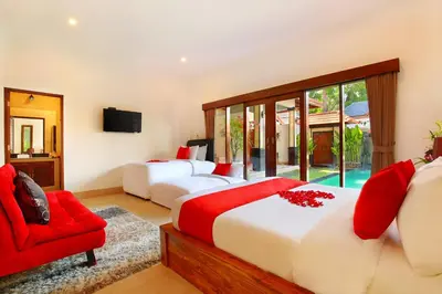 a bedroom with two beds and a red chair at De Liza Villa Seminyak Beachside By Bali Asia Villa in Seminyak