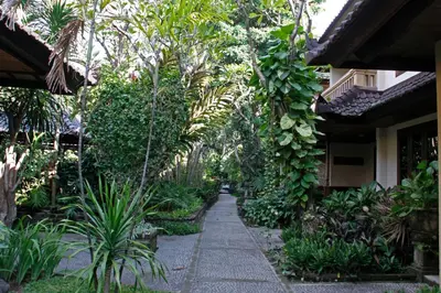 a garden with palm trees and a walkway at Hotel Puri Bambu in Jimbaran