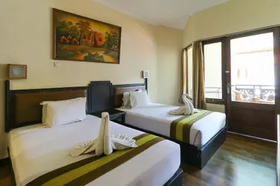 two beds in a hotel room with a window at The Flora Kuta Bali in Kuta