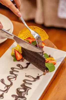 a person cutting a piece of chocolate cake with a fork at Sana Vie Villa Seminyak by Ini Vie Hospitality in Seminyak